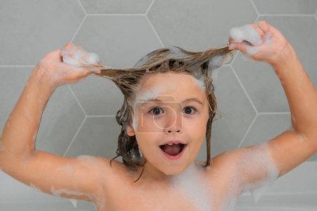 Foto de Niño lavando el cabello. Niño en un baño con espuma. Procedimientos de baño e higiene para niños. Bañera con burbuja de jabón. Cara divertida de los niños - Imagen libre de derechos