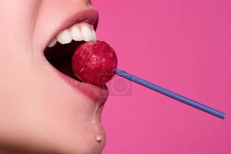 Photo for Closeup female lips with pink lipgloss holding in mouth red lollipop candy. Lollipop lips woman face - Royalty Free Image