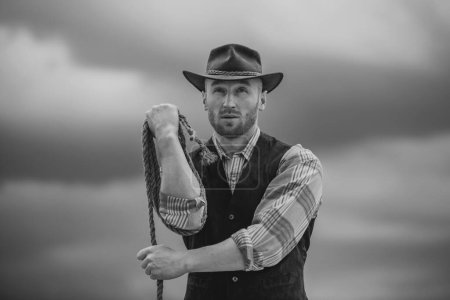 Photo for Sexy western man with cowboy hat. Cowboy with lasso rope on sky background - Royalty Free Image