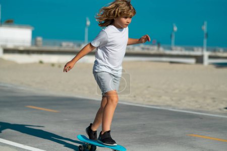 Foto de Patineta infantil en el parque de verano. Niño aprendiendo a montar skate board. Deporte activo al aire libre para niños. Patinaje infantil. Cabalgata en monopatín. Vamos a montar - Imagen libre de derechos