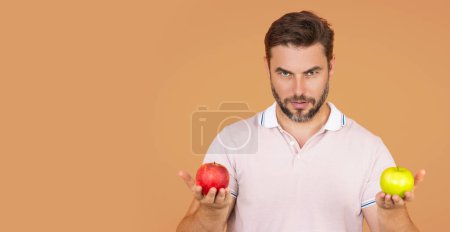 Téléchargez les photos : Concept de stomatologie. Homme tenant pomme sur fond beige studio isolé. L'homme mange de la pomme verte. Gros plan portrait de jeune homme aux pommes vertes et rouges. Alimentation saine. Bannière, espace de copie - en image libre de droit