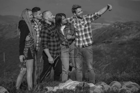 Téléchargez les photos : Groupe d'amis prenant un selfie dans les montagnes. Groupe de jeunes passent du temps libre ensemble, hommes heureux avec guitare et filles sur le camping - en image libre de droit