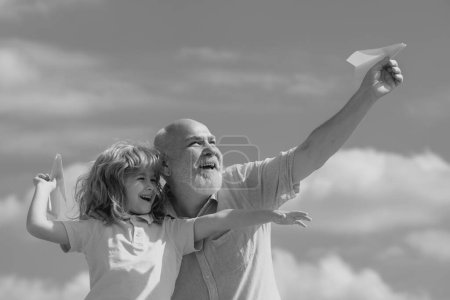 Foto de Nieto joven y abuelo viejo con avión de papel de juguete contra el fondo del cielo de verano. Niño con sueños de volar - Imagen libre de derechos