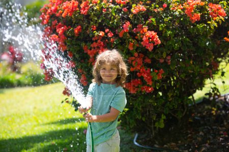 Photo for Child playing in garden, pours from the hose, makes a rain. Happy childhood concept - Royalty Free Image
