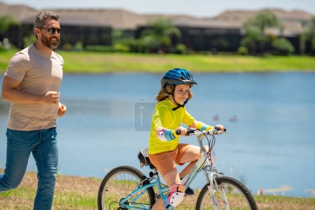 Photo for Happy Fathers day. Father and son in bike helmet for learning to ride bicycle at park. Father helping son cycling. Father and son on the bicycle on summer day. Kid son trying to ride bike with father - Royalty Free Image