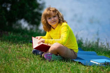 Foto de Niño inteligente lectura libro en el parque al aire libre. Niño rubio leyendo un libro en verano. Retrato al aire libre de niños inteligentes. Niños imaginación, innovación e inspiración. Escuela al aire libre, aprender niños - Imagen libre de derechos