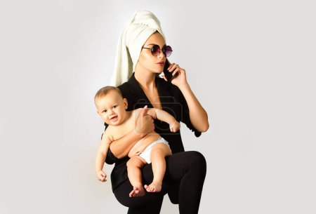 Foto de Mother business woman and her baby child in studio. Loving mom working with her child. Portrait of busy mum mother hugging her child. Mothers day for businesswoman - Imagen libre de derechos