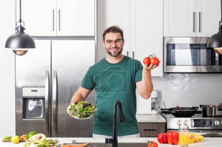 Photo for Man with vegetable salad in kitchen. Man cooking vegan healthy salad in kitchen. Man at modern kitchen with vegetables, prepare fresh vegetable salad for dinner or lunch. Healthy lunch or dinner - Royalty Free Image