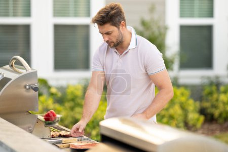 Photo for Man at a barbecue grill. Male cook preparing barbecue outdoors. Bbq meat, grill for picnic. Roasted beef. Cook preparing barbeque in the house yard. Barbecue and grill. Man using barbecue tongs - Royalty Free Image