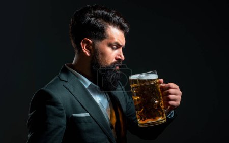 Téléchargez les photos : Un homme en costume classique buvant de la bière. Barbu gars en tenue de travail semble heureux et satisfait. Portrait profil de l'homme avec haut verre de bière levé sur fond noir - en image libre de droit