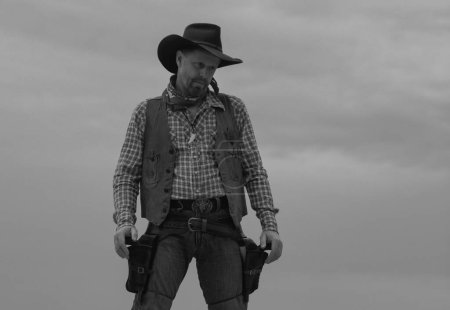 Foto de Vaquero con traje negro y sombrero de vaquero. Hombre con pistola de revólver West Vintage y munición de mariscal. Americano occidental, buscado - Imagen libre de derechos