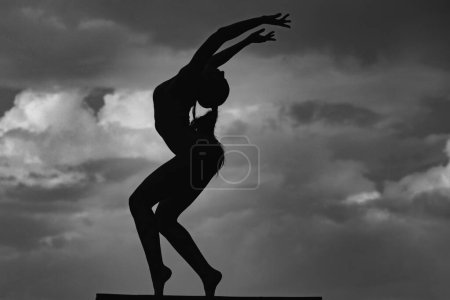 Photo for Silhouette of woman stretching. Young girl practicing yoga, doing fit exercise, working out. Dance studio. Cloudy sky background - Royalty Free Image