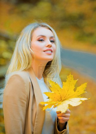 Téléchargez les photos : Tendance de la mode d'automne. Jeune belle femme marchant dans le parc tenant la feuille. Feuilles tombant, temps d'automne dans la nature - en image libre de droit