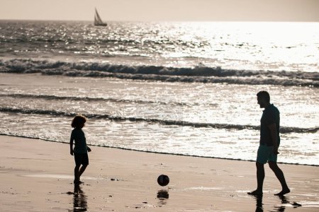 Téléchargez les photos : Père et fils jouent au football ou au football sur la plage. Voyage en famille, vacances, concept de fête des pères. Papa et enfant jouant en plein air - en image libre de droit