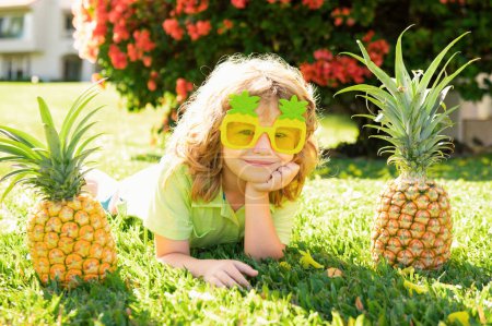 Foto de Niño sosteniendo una piña posando fondo de naturaleza de verano con espacio para copiar. Concepto de frutas saludables para niños - Imagen libre de derechos