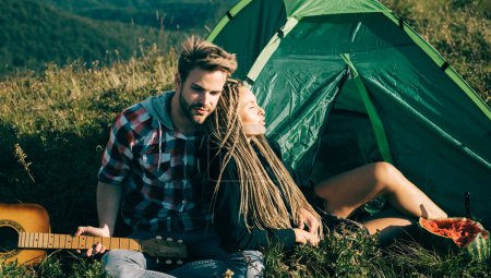 Foto de Pareja romántica enamorada de acampar al aire libre y sentada cerca de la tienda. Feliz hombre y mujer en unas vacaciones de camping románticas - Imagen libre de derechos