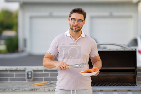 Photo for Cook man preparing barbecue grill outdoor. Man cooking tasty food on barbecue grill at backyard. Chef preparing food on barbecue. Millennial man grilling salmon fillet on grill. Bbq party - Royalty Free Image
