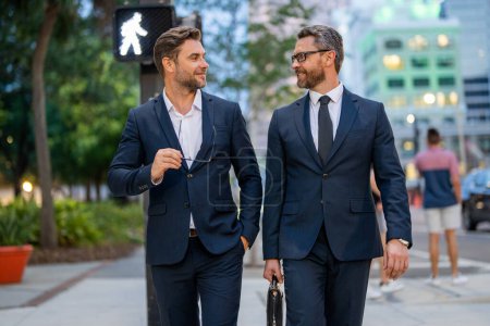 Photo for Two elegant businessmen walking outdoors together in the streets with office building. Business men walking outdoors together in the street discussing and chatting. Businessmen from work - Royalty Free Image