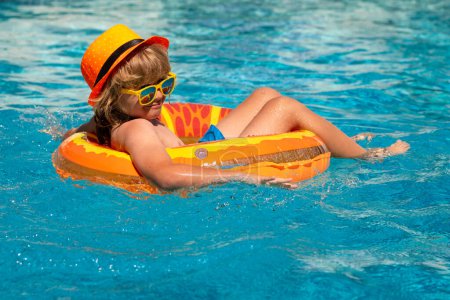 Foto de Niño nadando en la piscina jugar con anillo flotante. Sonriente lindo niño en gafas de sol nadar con anillos inflables en la piscina en el día de verano. Niño relajarse con anillo de piscina en la playa de agua de mar - Imagen libre de derechos