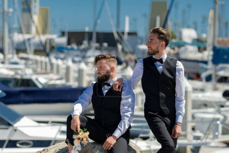 Photo for Gay man with partner on wedding day near yacht boat. Married LGBT couples celebrate a romantic wedding ceremony together with a bouquet flower. Portrait of gay couple in love on wedding day - Royalty Free Image