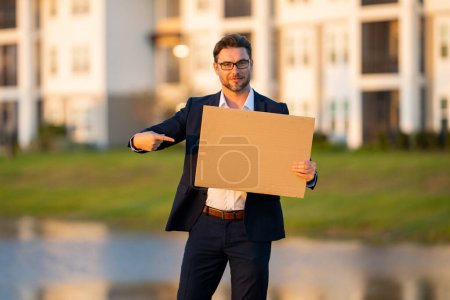 Photo for Handsome business man holding empty board and pointing finger. Man showing blank signboard with copyspace. Idea and offer. Your advertisement. Blank advertising board with empty space for text, mockup - Royalty Free Image