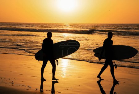 Foto de Playa tropical mar océano con puesta de sol o salida del sol para vacaciones de verano. Silueta de surfistas llevando su tabla de surf en la playa del atardecer. Paisaje marino - Imagen libre de derechos