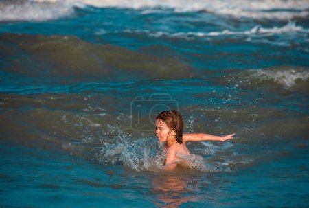 Téléchargez les photos : Les enfants heureux s'amusent en mer sur la plage. Océan bleu avec de grosses griffes blanches sur le fond. Enfant nageant dans la mer avec des griffes - en image libre de droit
