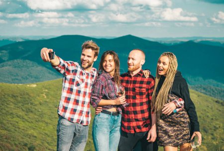 Foto de Un grupo de amigos tomando una selfie en las montañas. Grupo de excursionistas toma fotos en la naturaleza. Acampar juntos es diversión, amistad. Estudiantes en vacaciones de verano riendo y hablando - Imagen libre de derechos