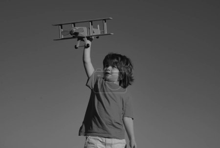 Foto de Niño niño de 7 años jugando con un avión de juguete de madera, sueña con convertirse en piloto. Sueños de niños. Aviador piloto infantil con avión de madera - Imagen libre de derechos