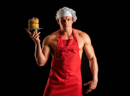 Téléchargez les photos : Homme sexy en chapeau de chefs avec une pile de crêpes maison sucrée avec du sirop. Chef muscle homme avec tablier pâtisserie crêpes aux baies et sirop d'érable - en image libre de droit