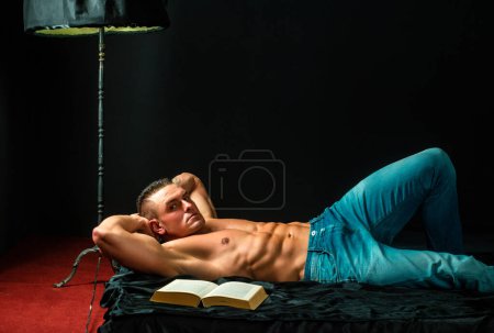 Téléchargez les photos : Un mec sexy dans la chambre. Homme au lit avec livre. Concept de sexe et relaxation. Amoureux du livre - en image libre de droit