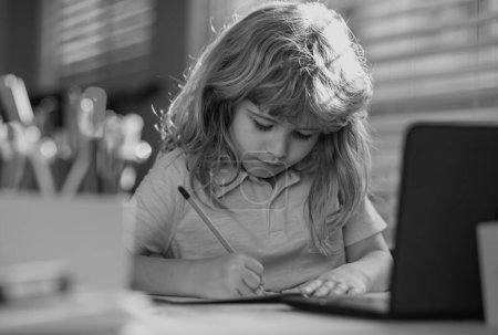 Photo for Child writing at school. A school age boy does homework at home. Portrait of little schoolboy sitting at table, doing homework. Smart child doing logic exercises alone at home - Royalty Free Image