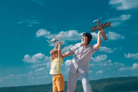 Téléchargez les photos : Petit-fils et grand-père avec avion et drone quadcopter sur fond bleu ciel et nuages - en image libre de droit