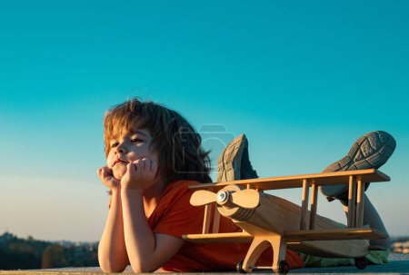 Téléchargez les photos : Enfant de 6 ans rêvant et joue avec un avion jouet dans le parc. Rêves de voyage. Développement, croissance, rêves et plans. Imagination et concept de rêve - en image libre de droit