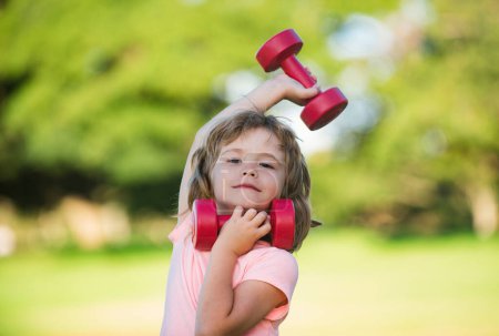 Téléchargez les photos : Enfant garçon fait des exercices avec des haltères dans le parc d'été. Activités saines mode de vie des enfants - en image libre de droit