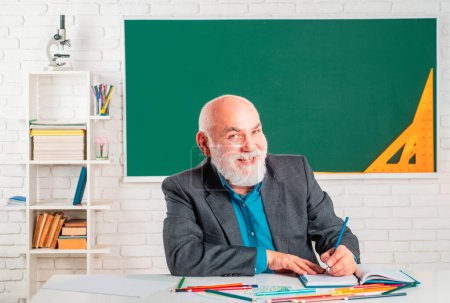 Photo for Portrait of happy senior teacher sitting in classroom. Cheerful teacher who loves his job. Funny old professor. Smiling teacher - Royalty Free Image