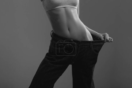 Téléchargez les photos : Woman with her big trousers after successful diet and weight loss. Weight loss concept, girl showing her progress of losing weight - en image libre de droit