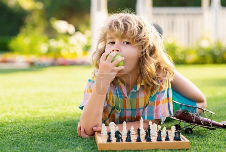 Téléchargez les photos : Intelligent concentré et pensant gamin jouer aux échecs et manger de la pomme - en image libre de droit