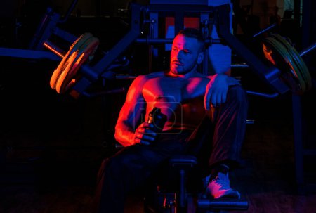 Photo for Tired sporty man resting after training. Man with bottle of water or protein on neon background. Shirtless man man with muscles torso, in the gym - Royalty Free Image