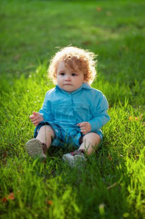 Téléchargez les photos : Portrait d'un petit garçon assis sur l'herbe jouant en plein air dans l'herbe - en image libre de droit