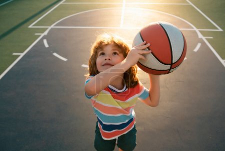 Téléchargez les photos : Joyeux petit garçon jouant au basket sur une aire de jeux. Sport pour enfants - en image libre de droit