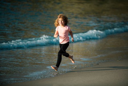 Foto de Chico feliz corre al mar. Niño divertirse en la playa, correr por la piscina de agua de mar. Vacaciones de verano con niño - Imagen libre de derechos
