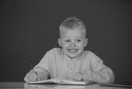 Photo for Funny face of little student of primary school study in classroom at school. Kid writing in notebook in class - Royalty Free Image
