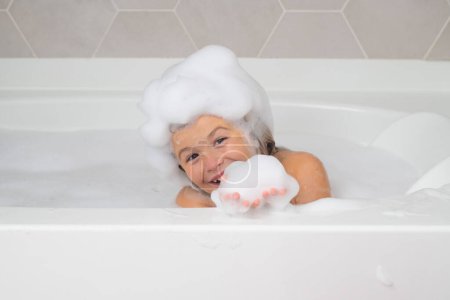 Foto de Cara de niños en espuma. Lindo lavado y baño de niños en un baño con espuma. Funny cara de niño bañado en el baño - Imagen libre de derechos