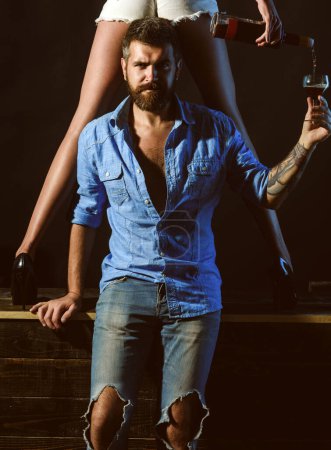 Téléchargez les photos : Couple jouant avec des jambes sexy. Un bel homme tenant une jambe de femme dans des chaussures élégantes. Couple sexy dégustation de vin - en image libre de droit