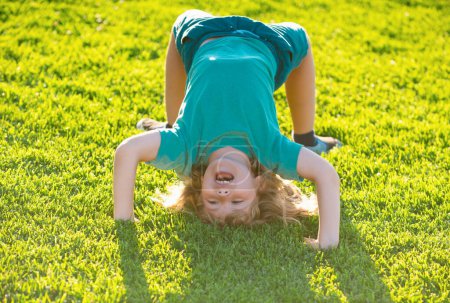 Téléchargez les photos : Happy kid garçon fille debout à l'envers sur sa tête sur l'herbe dans la journée d'été - en image libre de droit