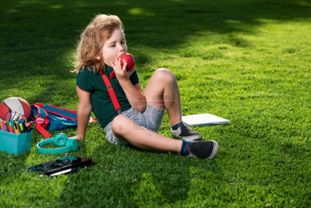 Foto de Educación para niños al aire libre. Niño haciendo tareas al aire libre y comiendo manzana - Imagen libre de derechos