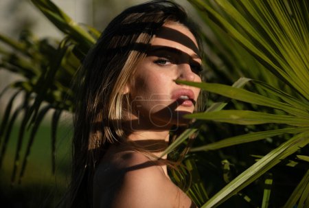 Photo for Closeup portrait of young and beautiful woman with perfect smooth tanned skin in tropical leaves. Concept of summer natural cosmetics and skincare. Girl face in palm leaves, exotic tropics cosmetics - Royalty Free Image