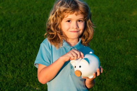 Photo for Boy putting money into a piggy bank. Portrait of a joyful cute little kid holding saving piggybank - Royalty Free Image