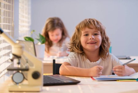 Foto de Niño de la escuela sentado en la mesa, escribiendo deberes o preparándose para el examen. Feliz niño sonriente estudio. Poco aprendizaje de los estudiantes - Imagen libre de derechos